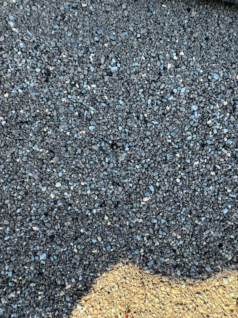 Shingle surface showing granule loss with exposed dark asphalt mat