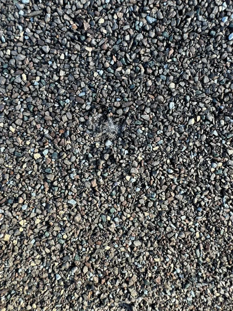 Close-up of loose roof granules showing coarse sandy texture