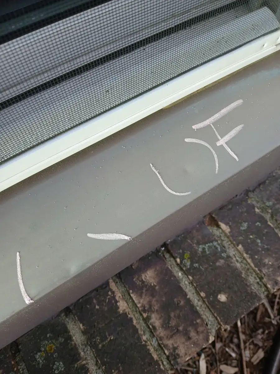 Chalk marks along a dented aluminum gutter with a screen on top