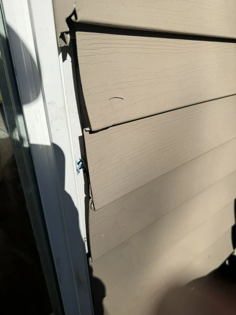 Storm-damaged vinyl siding showing cracking near window trim