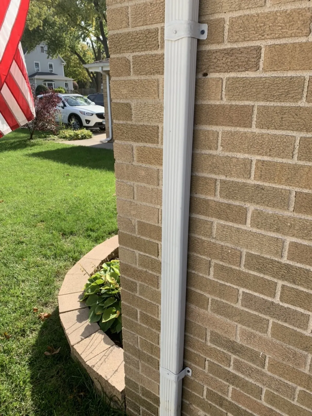 A white downspout installed on a brick exterior wall in Addison, IL