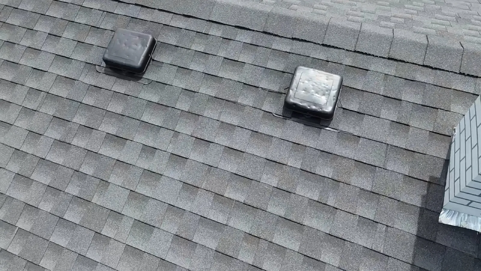 A close-up view of a gray asphalt architectural shingle roof with installed roof vents in Darien, IL