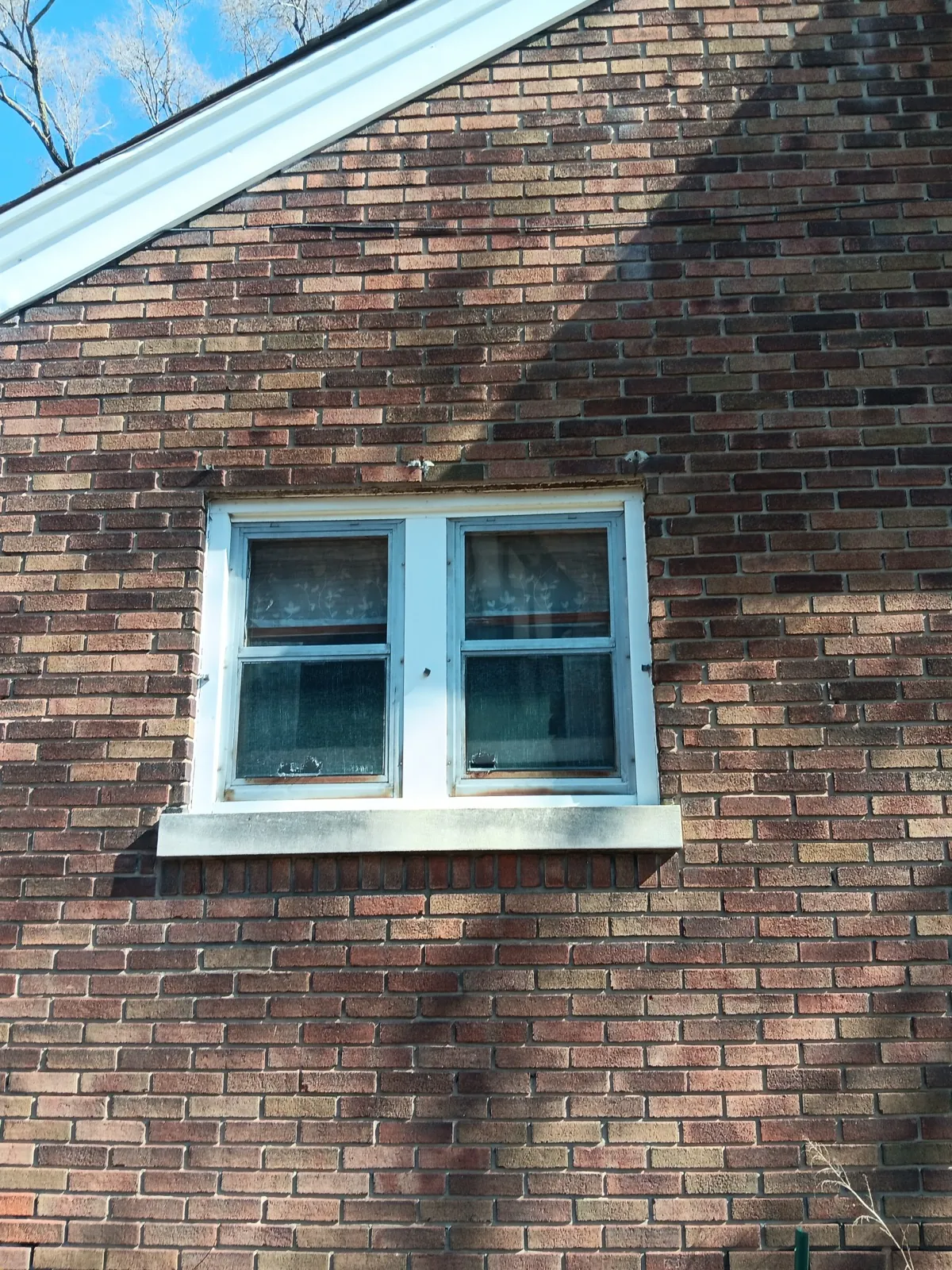 A close-up view of a brick exterior wall with a white-framed window in Elgin, IL