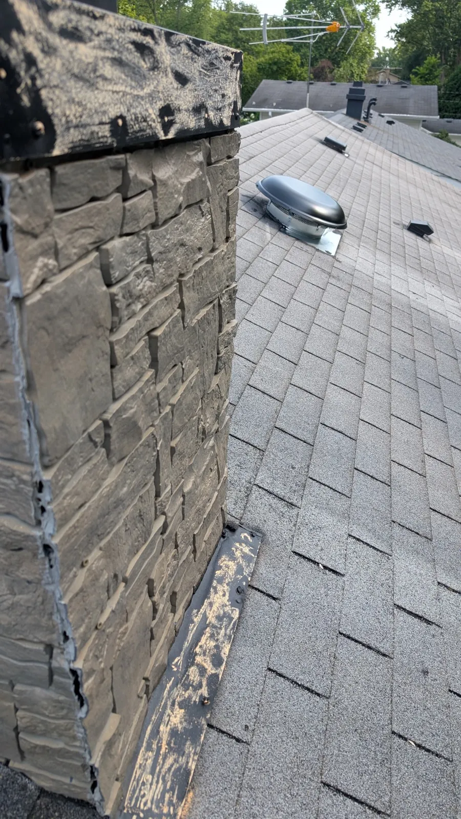 A close-up view of a new asphalt shingle roof meeting a stone chimney in Geneva, IL