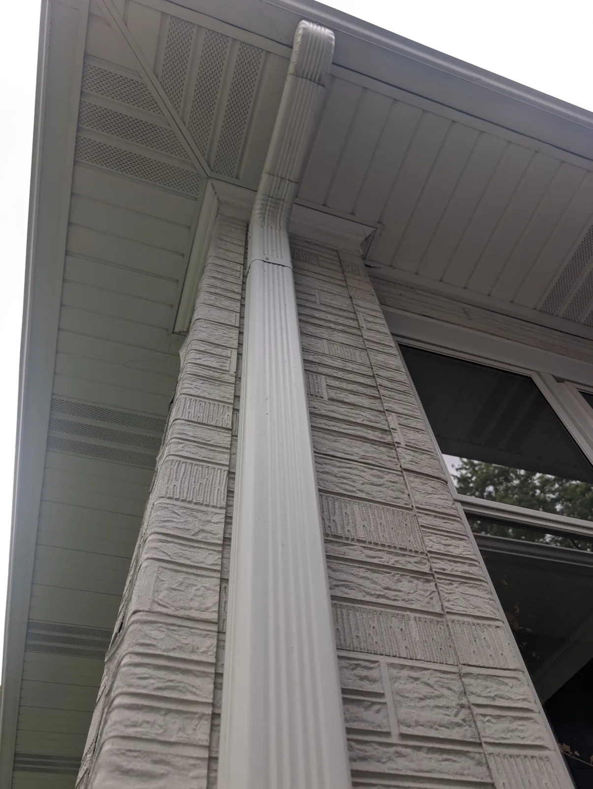 A white seamless gutter and downspout installed on a stone-textured exterior wall in River Forest, IL