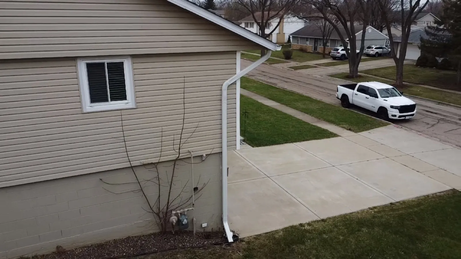 White aluminum gutters and downspouts installed on a house with beige siding in Streamwood, IL